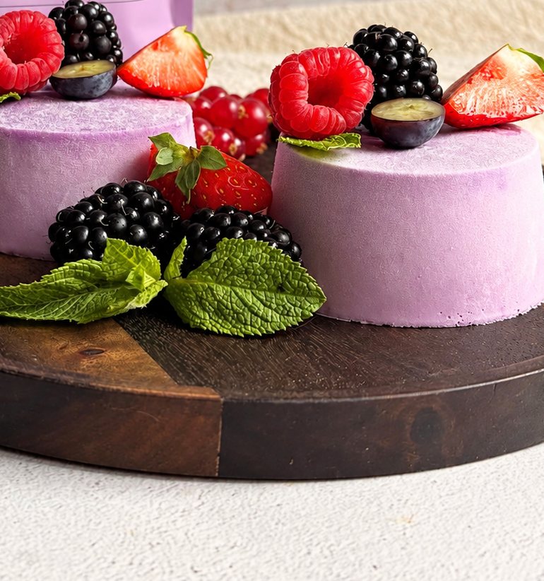 Twee paarse ube panna cotta's op een houten bord met frambozen, bramen, aardbeien en munt